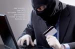Zamaskowany mężczyzna siedzi przy biurku z laptopem. W dłoni trzyma kartę kredytową
